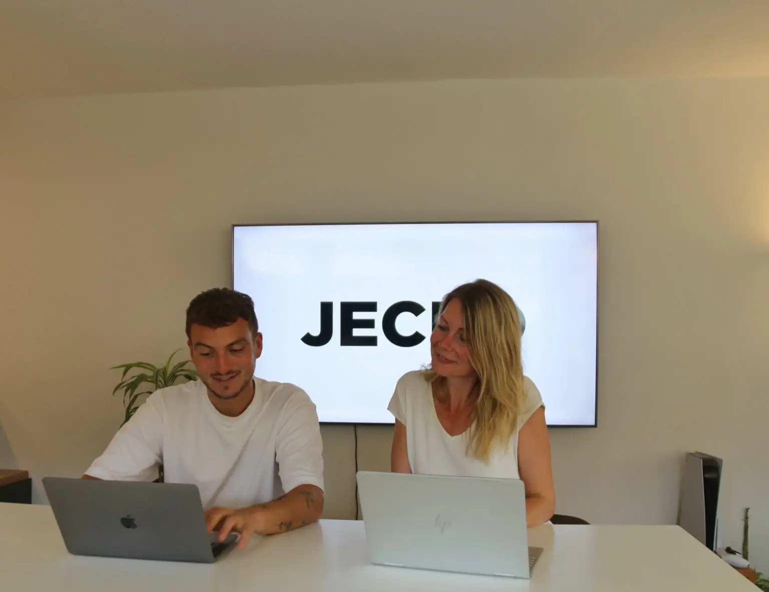 Twee teamleden van Jecko werken bij een tv-scherm met JECKO-logo